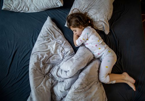 A little girl sleeping in a bed with blanket and pillows askew
