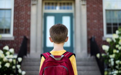 一个小男孩背着书包站在学校大楼前