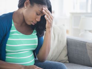 焦虑的黑人孕妇在沙发上摩擦额头