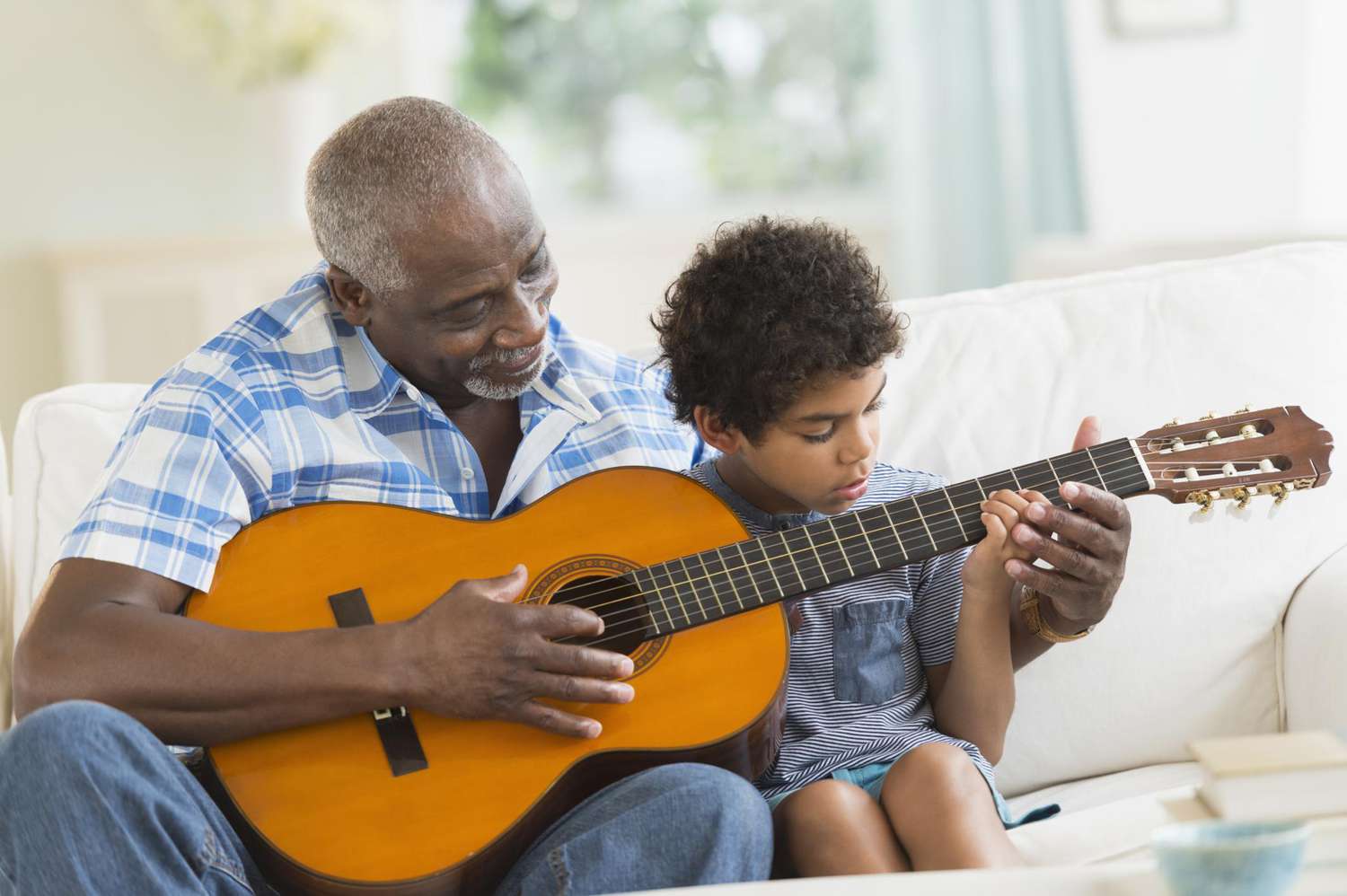 Boy playing guitar with grandfather on couch