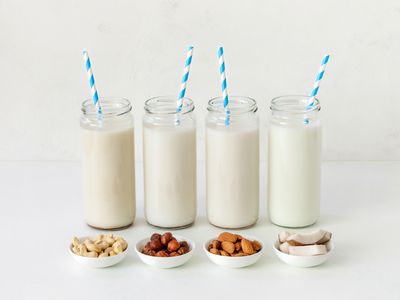 A vignette of four jars with non-dairy milk have blue and white striped straws.