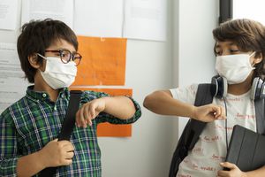两名戴着口罩、拿着学习用品的学生撞在一起。