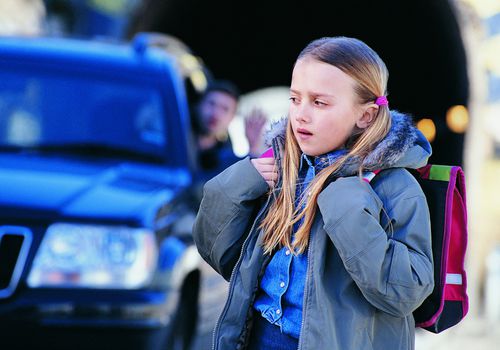 Man in car waving to apprehensive girl standing in the street