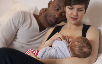 Happy young parents, mother is breastfeeding their newborn baby