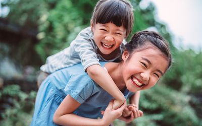 女孩抱着她的小妹妹开心地回到公园”width=