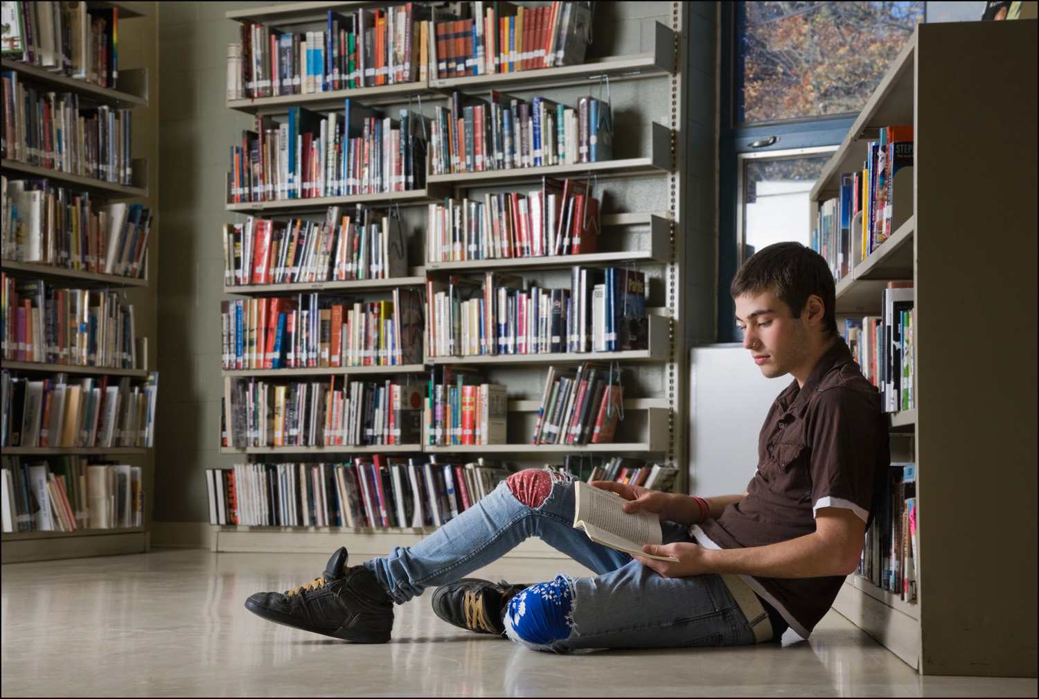 Teenage boy reading on the floor of a library