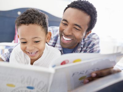 Happy father and son reading book together in bed