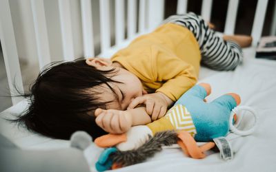 吮拇指的孩子睡在婴儿床旁边的毛绒玩具