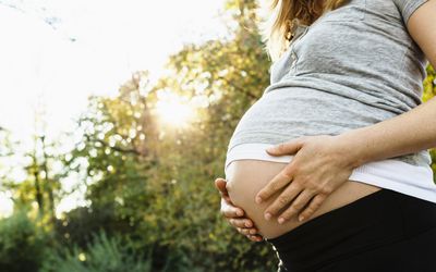 Pregnant woman holding belly, outdoors, mid section