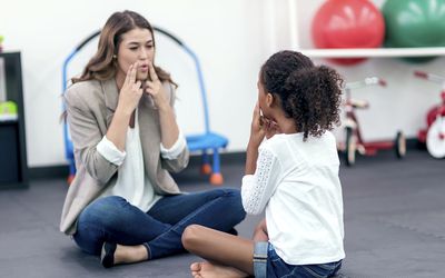 Adult female therapist guiding young girl in speech therapy
