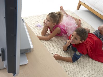 two children watching tv while wearing Halloween costumes