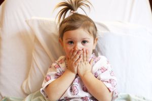 toddler in hospital bed covering her mouth