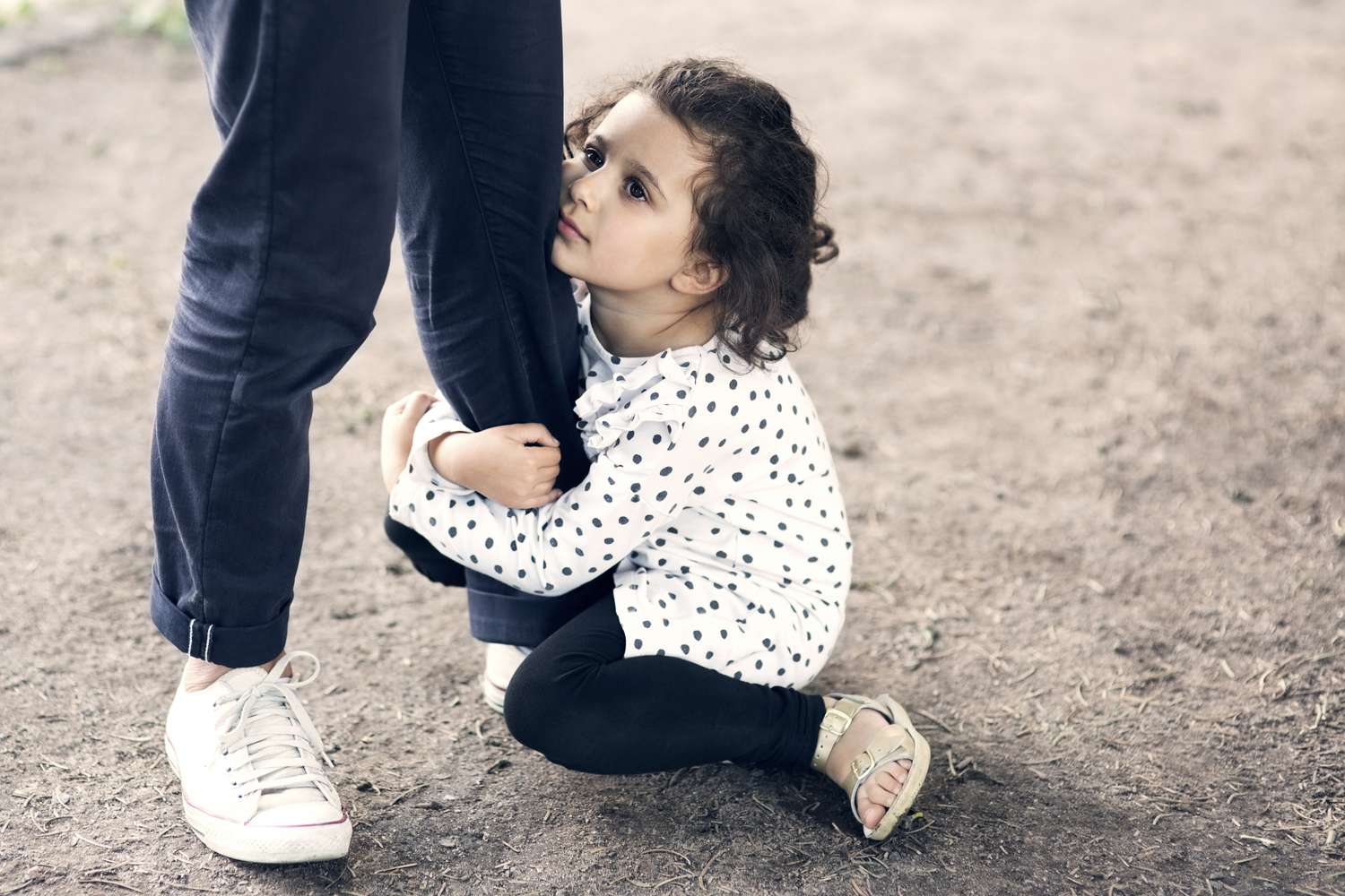Daughter gripping fathers leg while sitting on ground at park