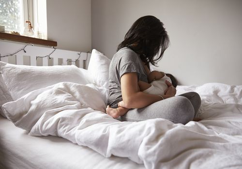 一名妇女坐在床上给婴儿喂奶