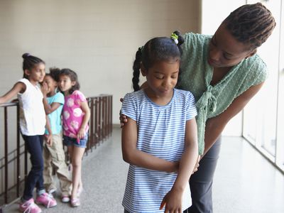 Teacher talking to bullied young girl while three other girls gossip in background