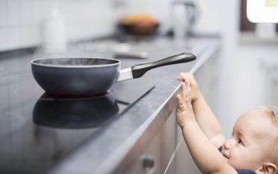 小男孩试图够到炉子上的平底锅