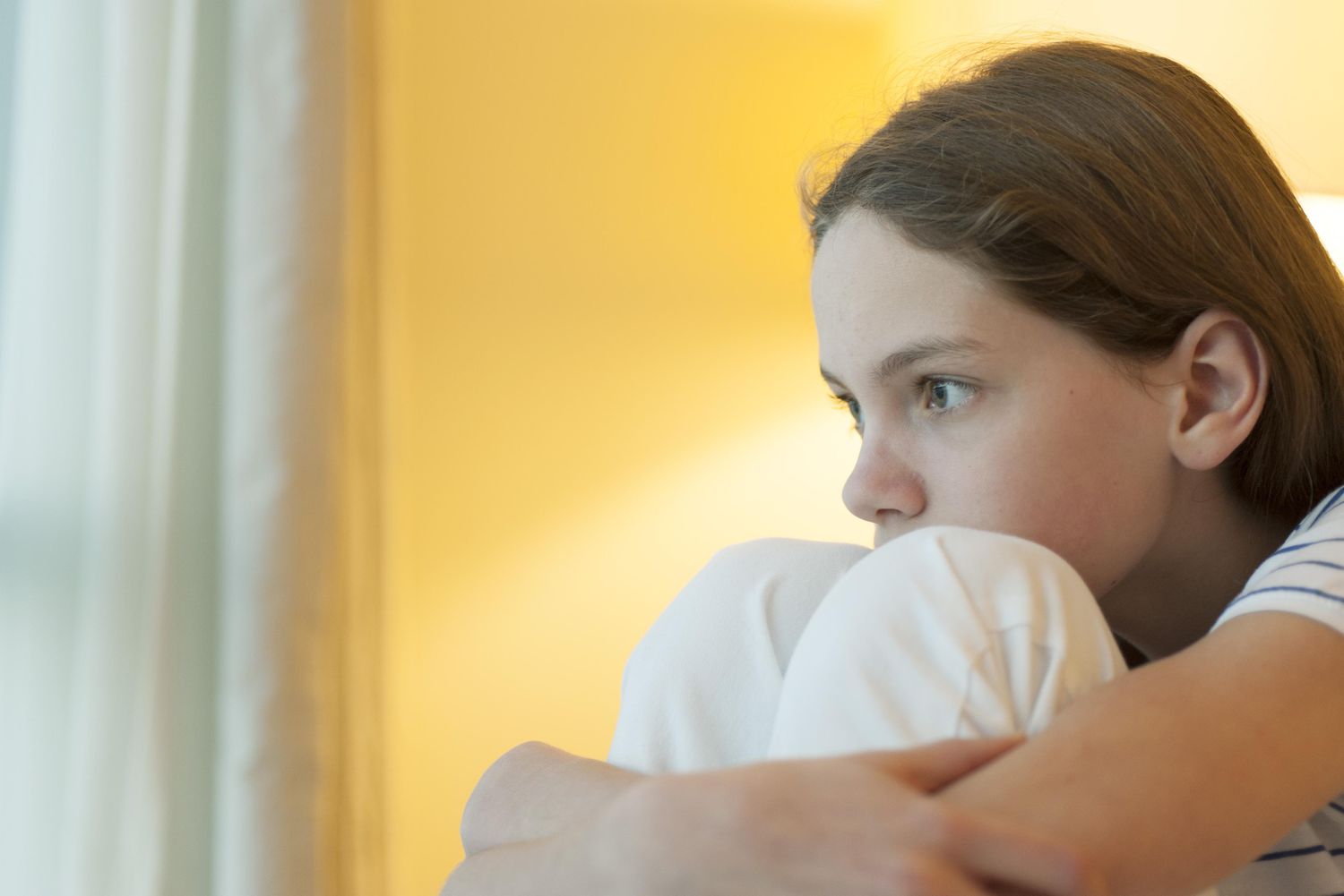 Preteen girl hugging knees, looking away in thought
