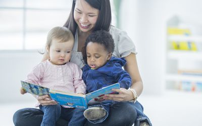 一个保姆拿着一本书给两个小孩读书