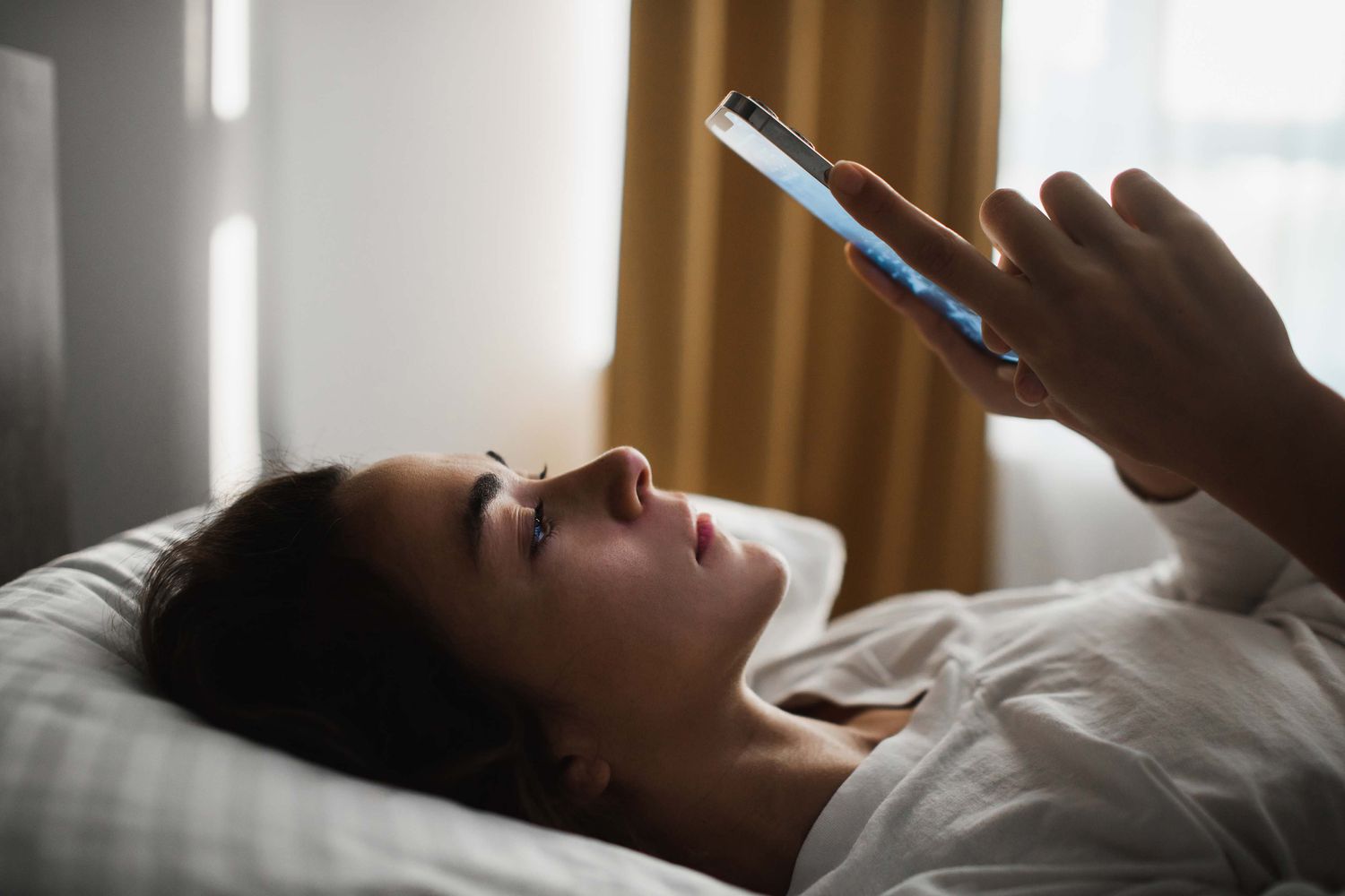 Sad and tired woman lying in bed with phone