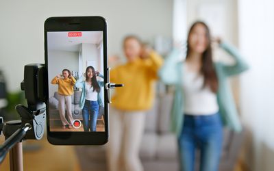Young woman with her friend creating dancing video by smartphone camera