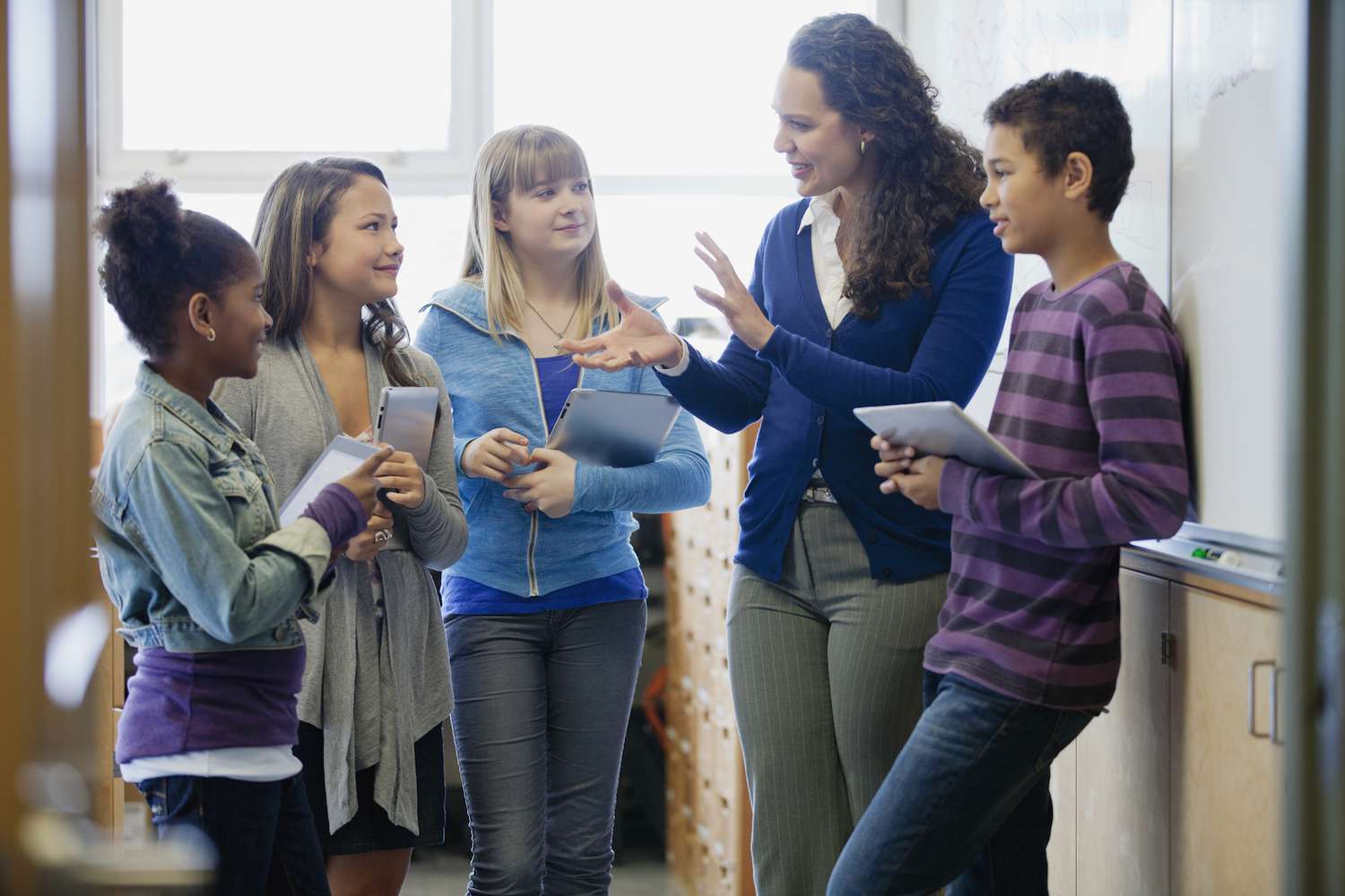 Middle school students talking with teacher in classroom