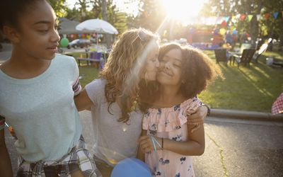 Affectionate mother kissing daughters cheek at summer neighborhood block party in park