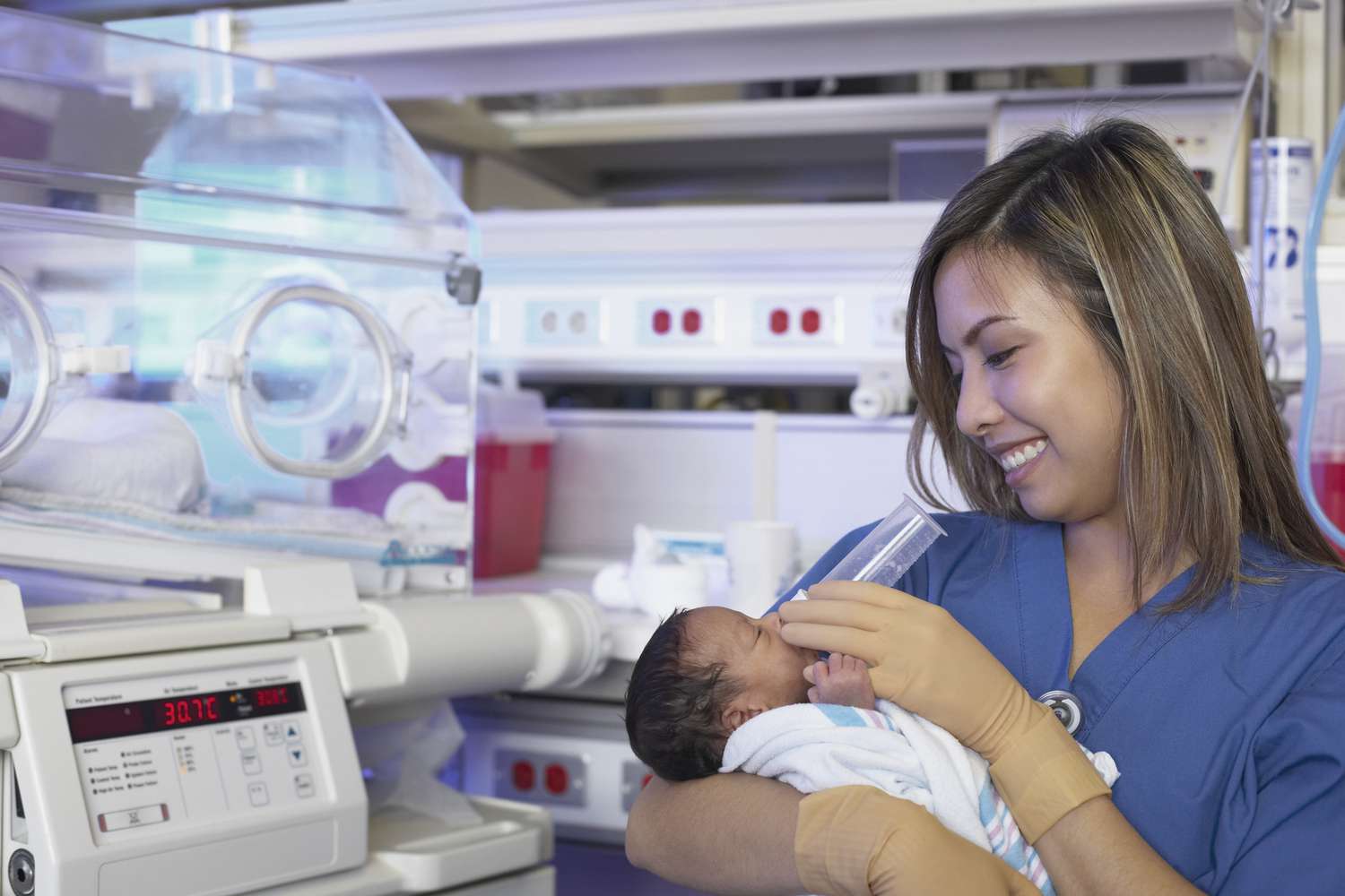 护士在保温箱旁给新生婴儿喂食