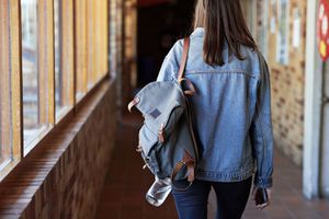 背着背包走在大学走廊的年轻女子的后视图