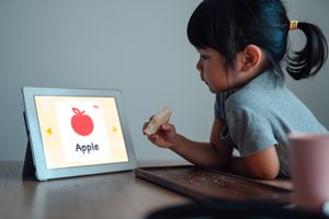 Young girl using a tablet in a case while eating at a table