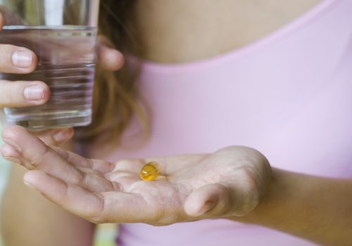 年轻女子拿着维生素药丸和一杯水，裁剪