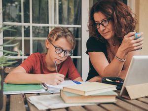 年轻的学生在家里用课本、报纸、电子记事本做作业。妈妈控制、帮助和教育儿子。教育，家庭，生活方式和在家上学的概念。