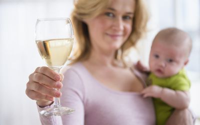 Model poses as a mother holding a baby and a glass of wine