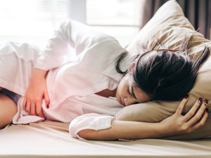 一名妇女躺在家里的床上疼痛地抚摸腹部