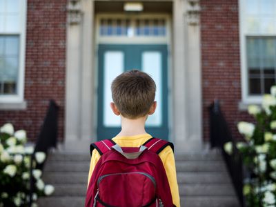 小男孩背着背包站在教学楼前