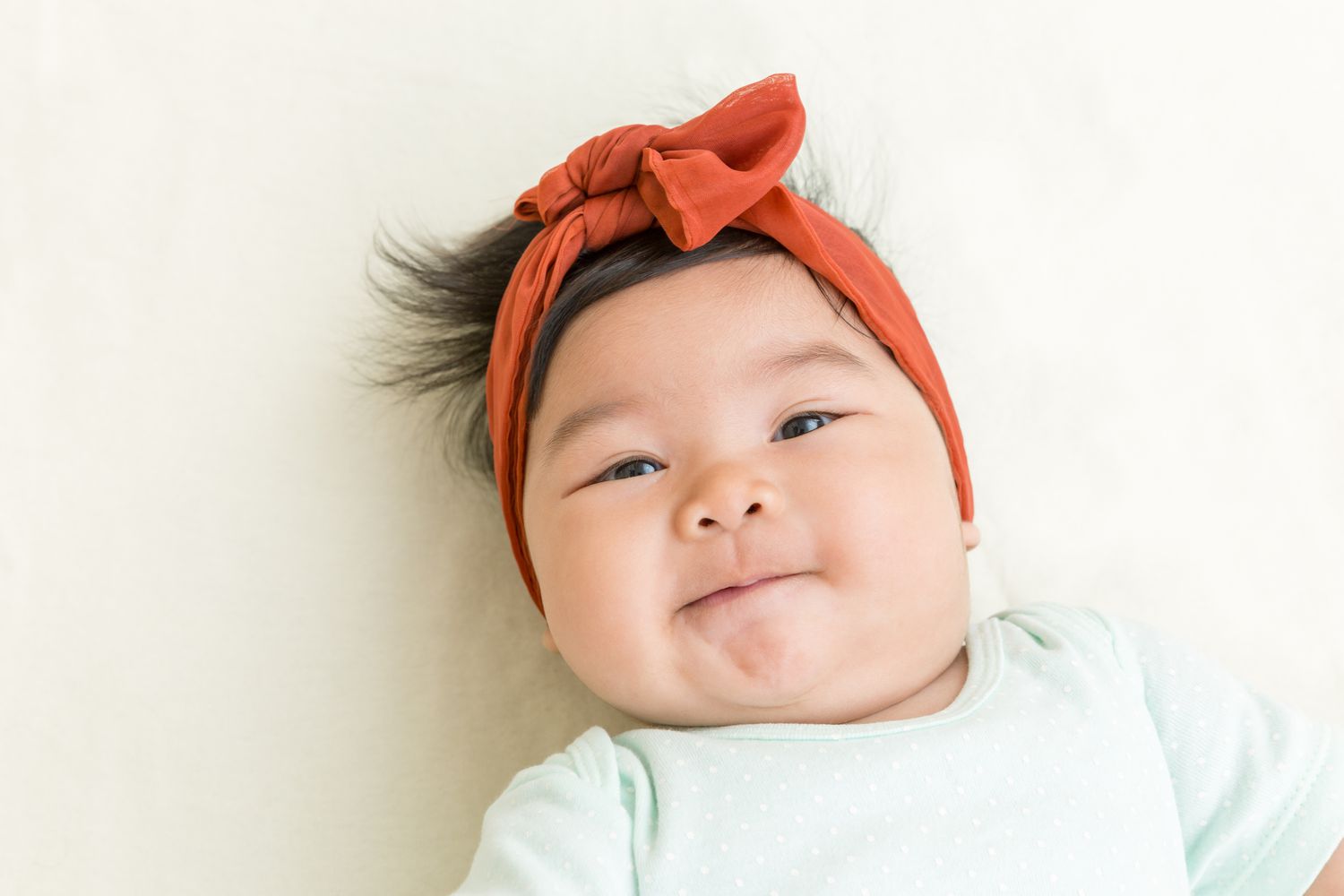 Baby girl with burnt orange headband and mint onesie looking at camera