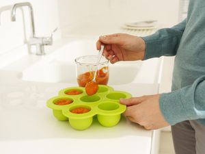 一个人用勺子舀着婴儿食品放在托盘里准备冷冻