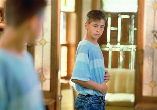 fitness and puberty - teen boy looking in mirror
