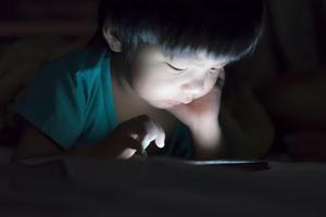 孩子拿着平板电脑在黑暗中躺在床上，晚上看书。