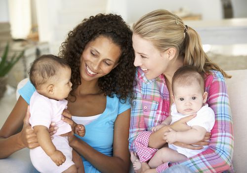 Two young mothers sitting on sofa at home with their babies
