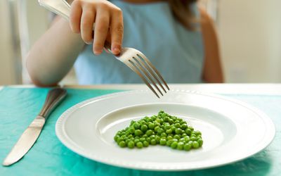 女孩用叉子吃青豆。