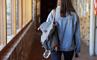 背着背包走在大学走廊的年轻女子的后视图