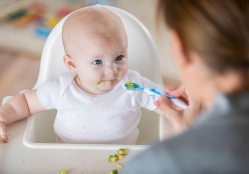 Unrecognizable mom feeds baby with spoon