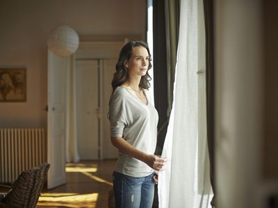年轻女子看着窗外的公寓-股票照片